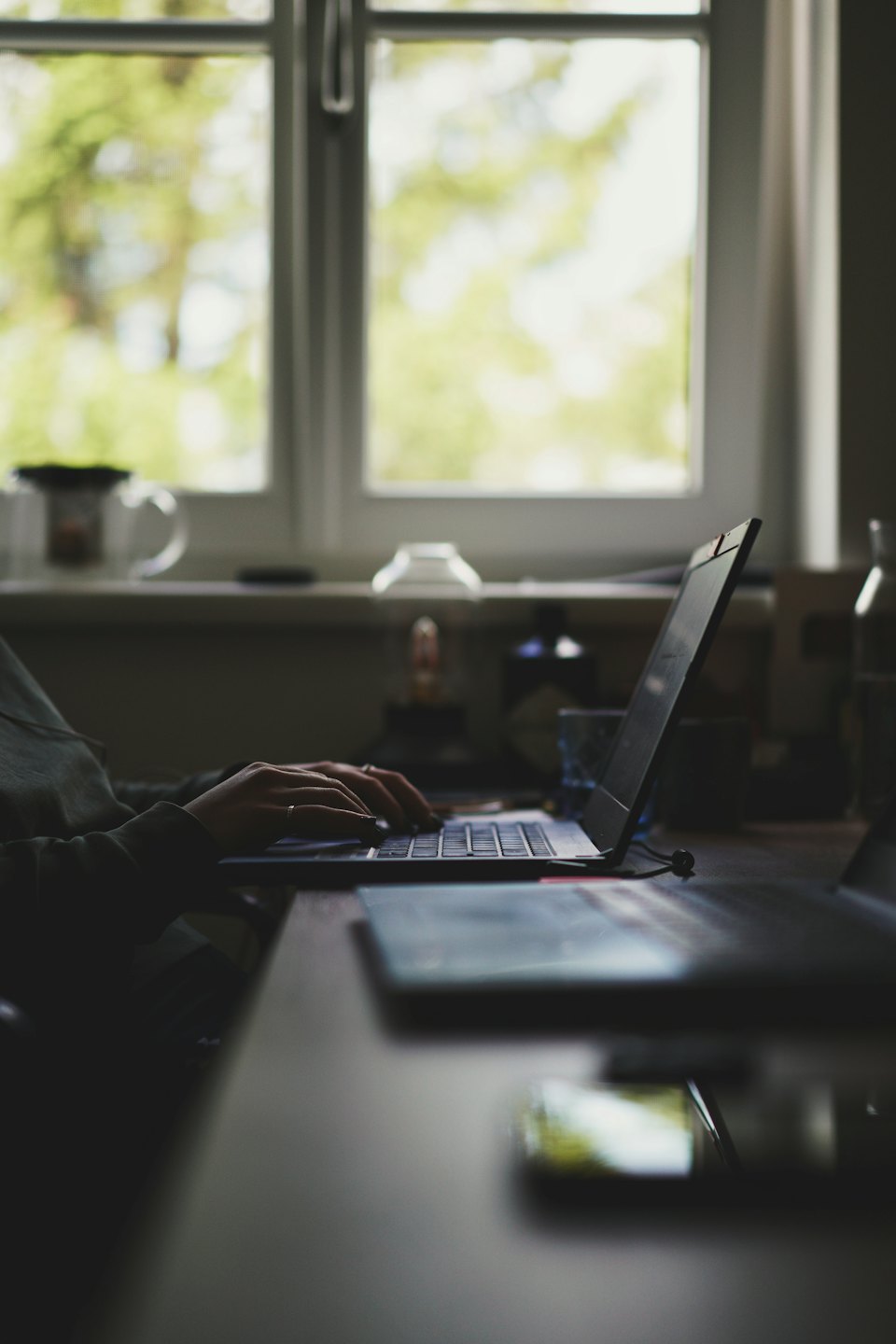 A person types on a laptop at a wooden desk.